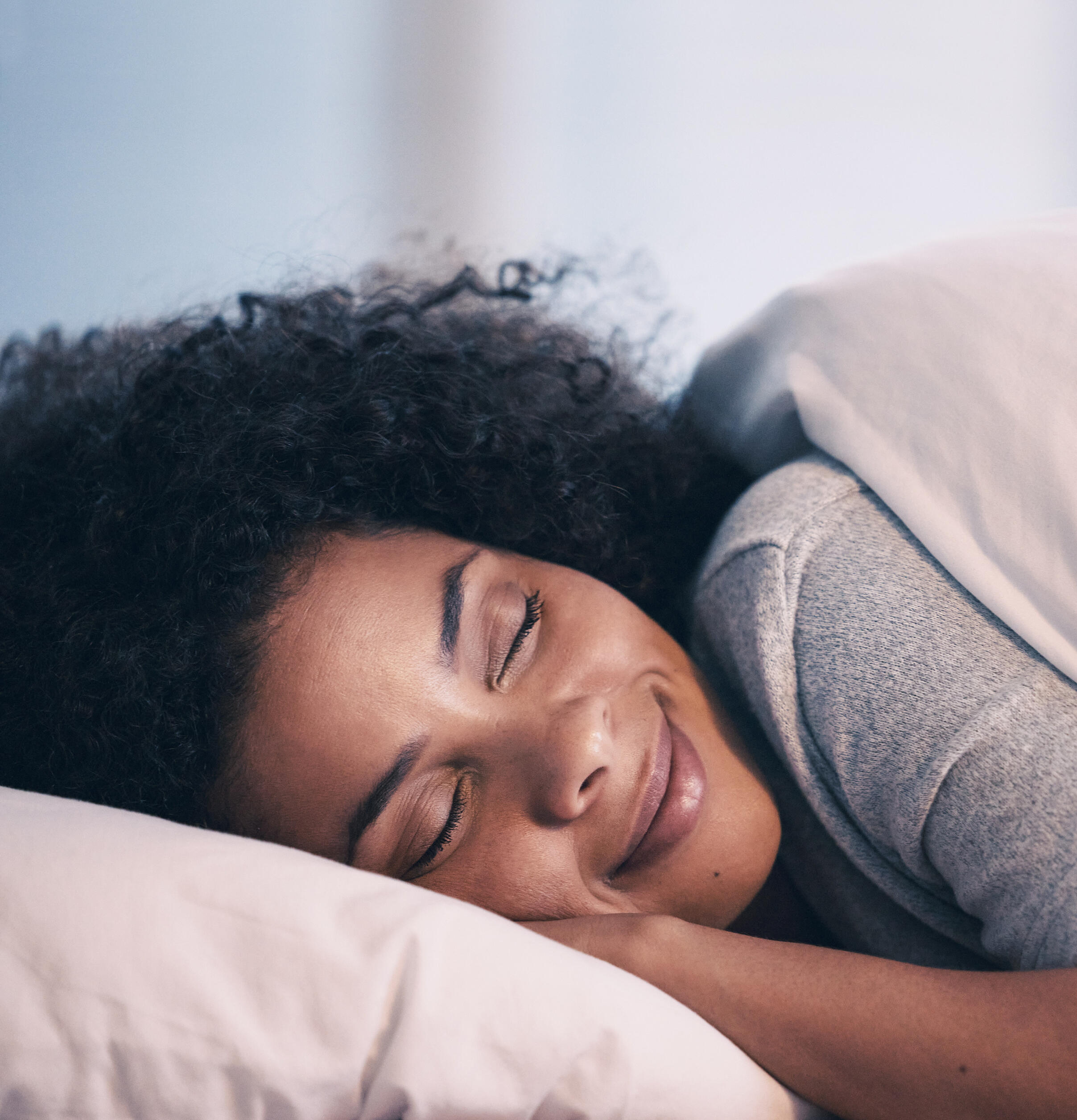The 92% Sleep Like This! ABiAn™ woman restfully smiling, eyes closed, head on pillow, hand under head, lying down.
